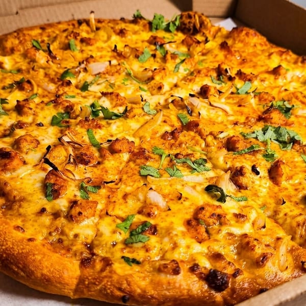 A whole chicken tikka pizza with cilantro and onions in a cardboard delivery box.