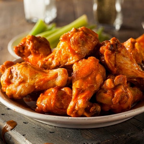 A plate of buffalo chicken wings with celery sticks, dipping sauce, and a glass of beer.