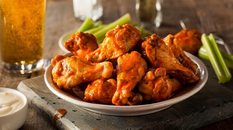 A plate of buffalo chicken wings with celery sticks, dipping sauce, and a glass of beer.