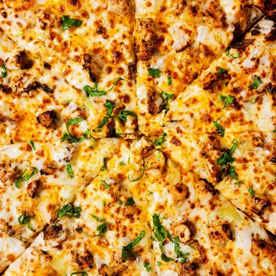 Close-up of a whole chicken pizza with melted cheese and green herbs in a cardboard box.
